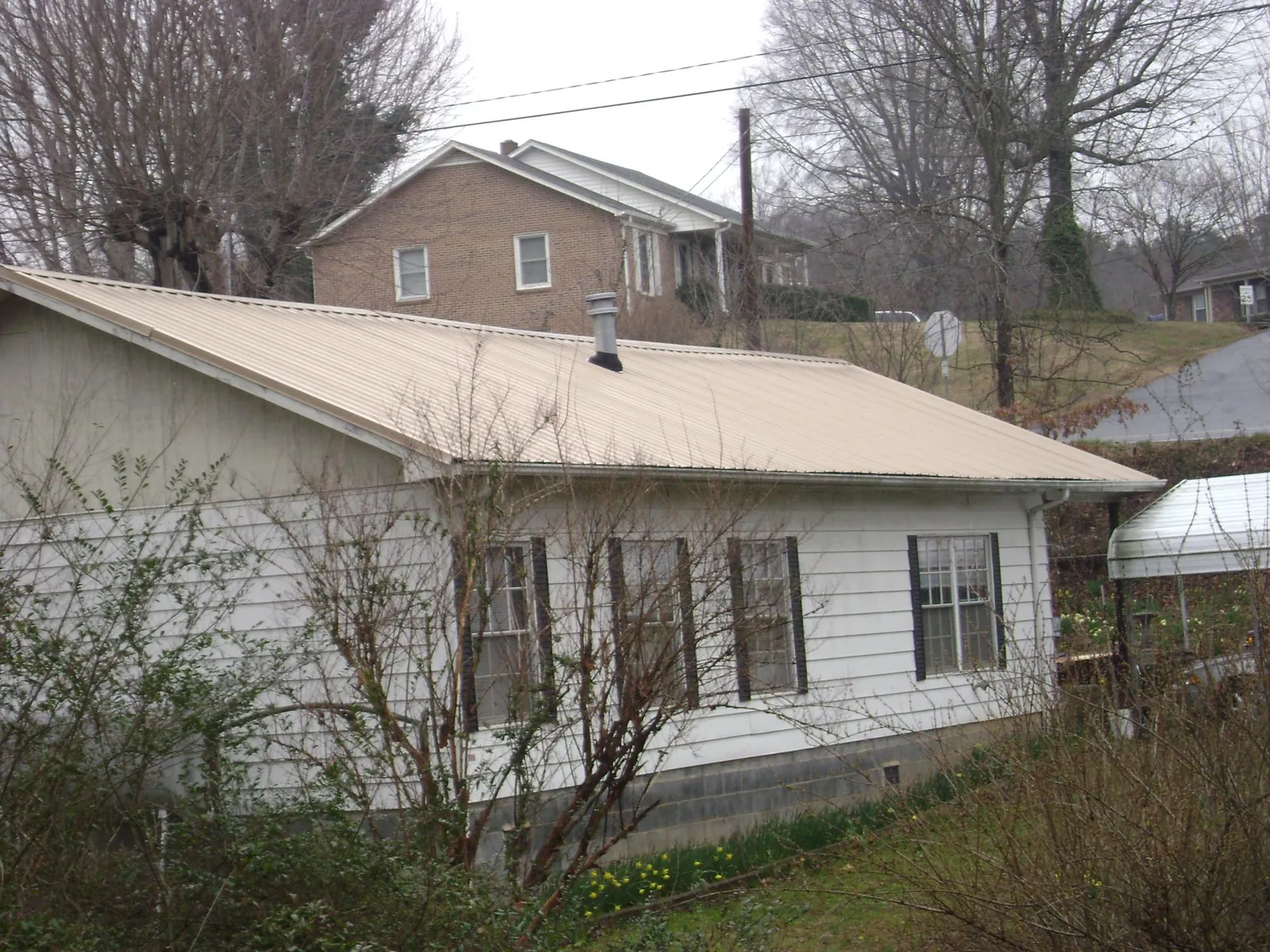 Tan metal roof on a white sided house set into a hillside — Commercial Roofing by Roofing Brothers in Bath